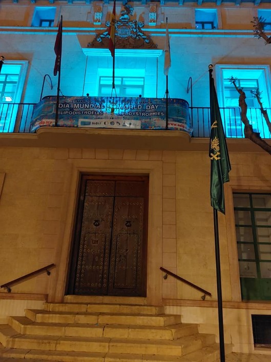 La fachada principal del Ayuntamiento de Totana se ilumina de color turquesa  con motivo del Día Mundial de las Lipodistrofias